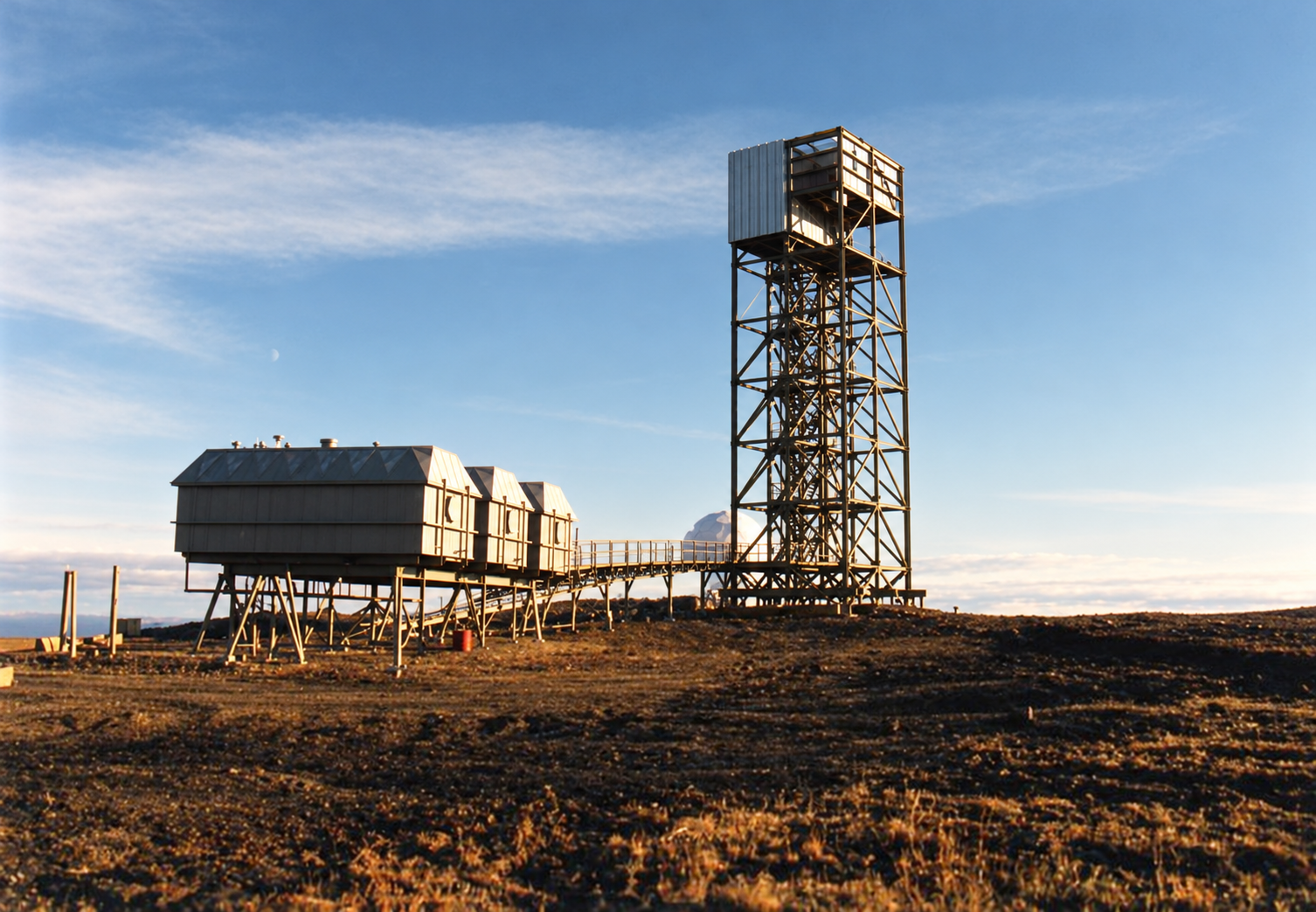 Interpretive view of North Warning System construction at Nicholson Peninsula, showing a skeletal short-range radar tower, raised equipment modules and the old DEW Line radome in the distance
