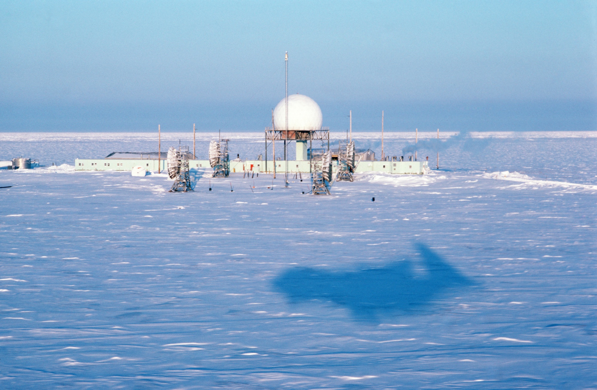 1987 aerial photograph of Oliktok POW-2 with radar radome and station buildings on the snowy Beaufort Sea coast