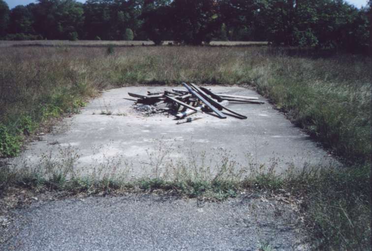 A small building foundation at the end of a curved asphalt road that came from the Barracks
