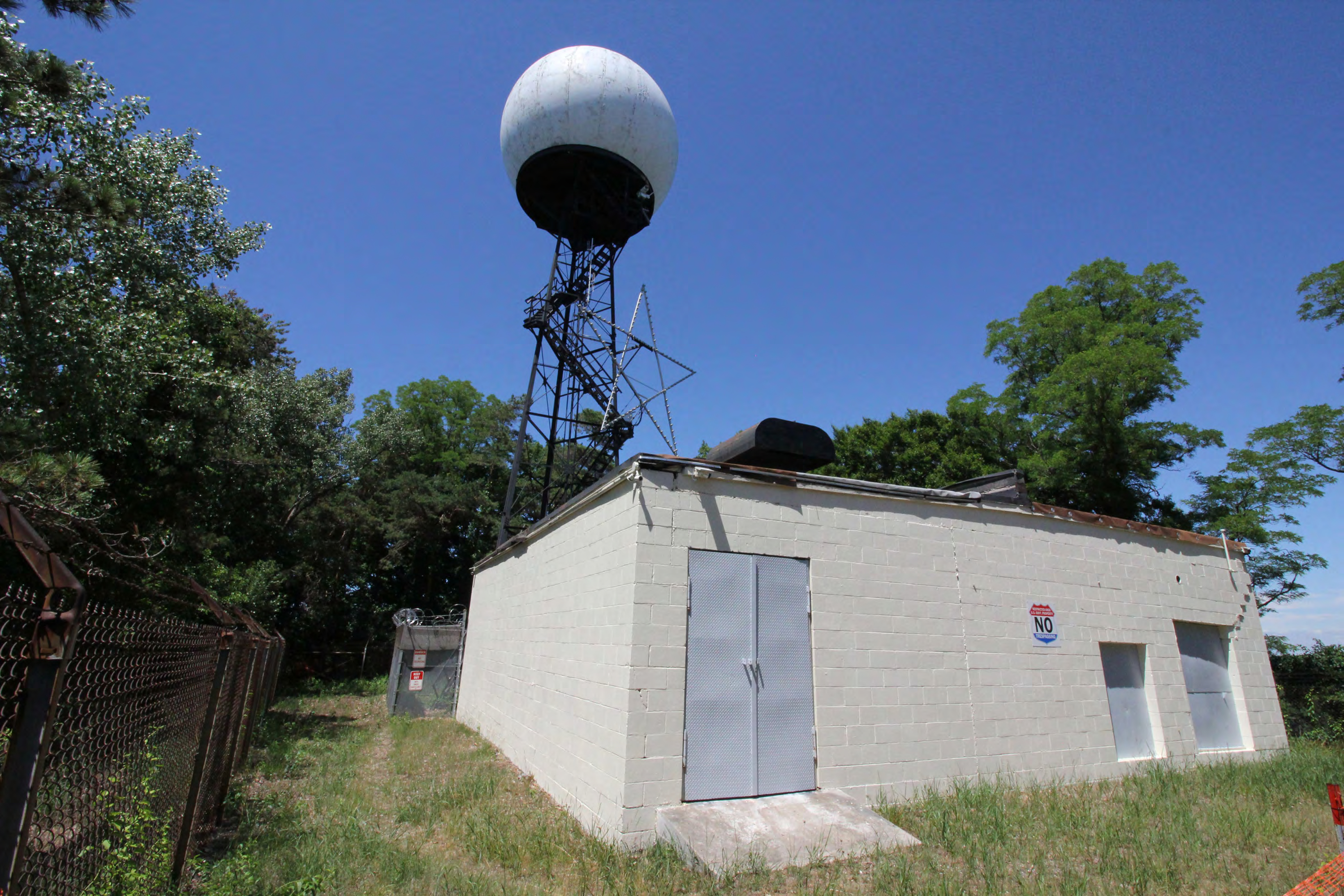 Equipment and generator building, west fence line, antenna tower security fence, antenna tower, from southwest