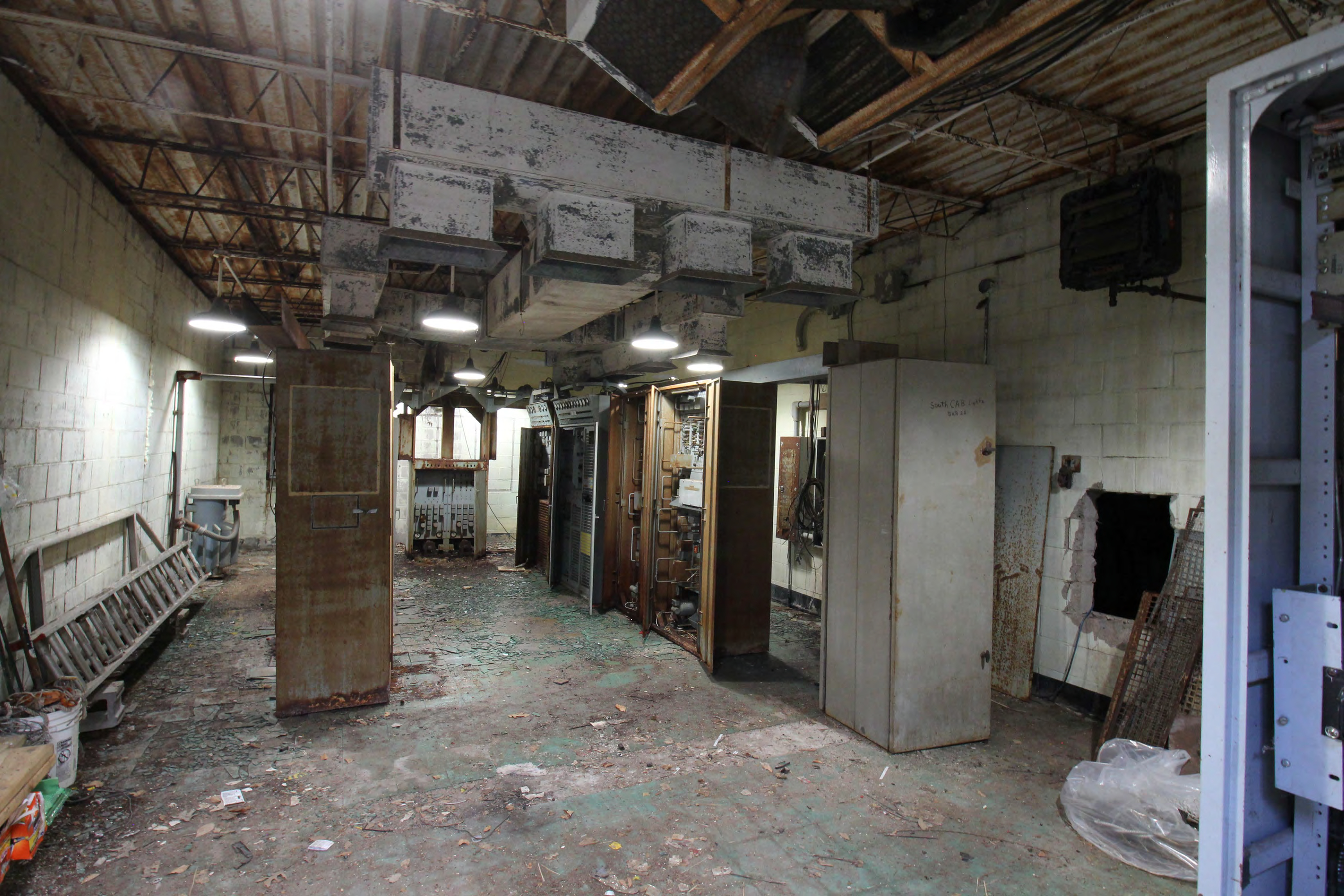 Equipment room from door, foreground to background; telephone cabinet, opening to generator room, FSW-1 Control Monitor Set, FPS-18 cabinet rows, FPS-18 Control Monitor, voltage regulating transformer (west/left wall), one of two.