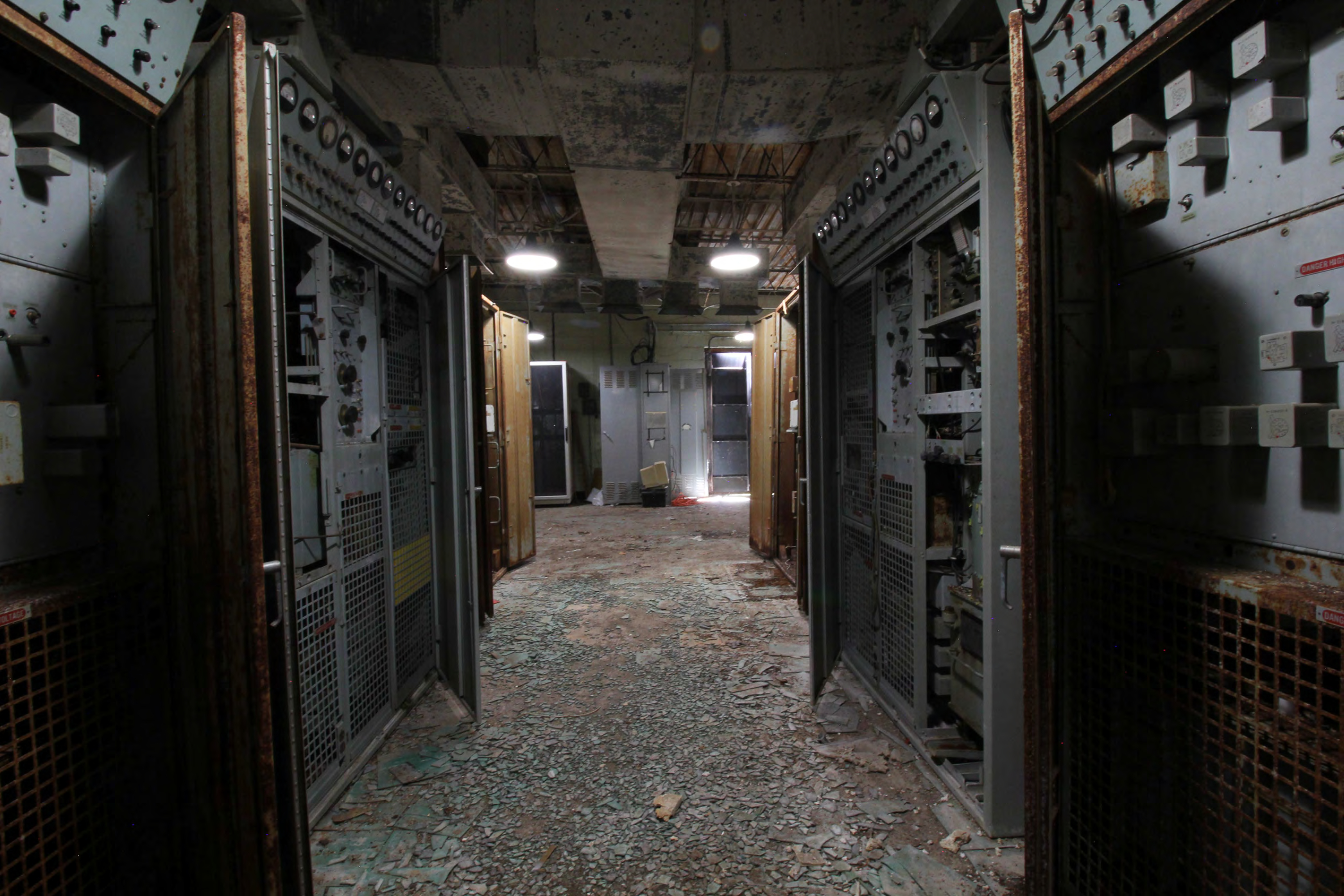 Equipment room from north, foreground; transmitter power supplies, transmitters, receivers and other cabinets not clearly visible. Background right to left; door, telephone equipment cabinet with doors open and relatively modern computer monitor in front, modern computer equipment cabinet