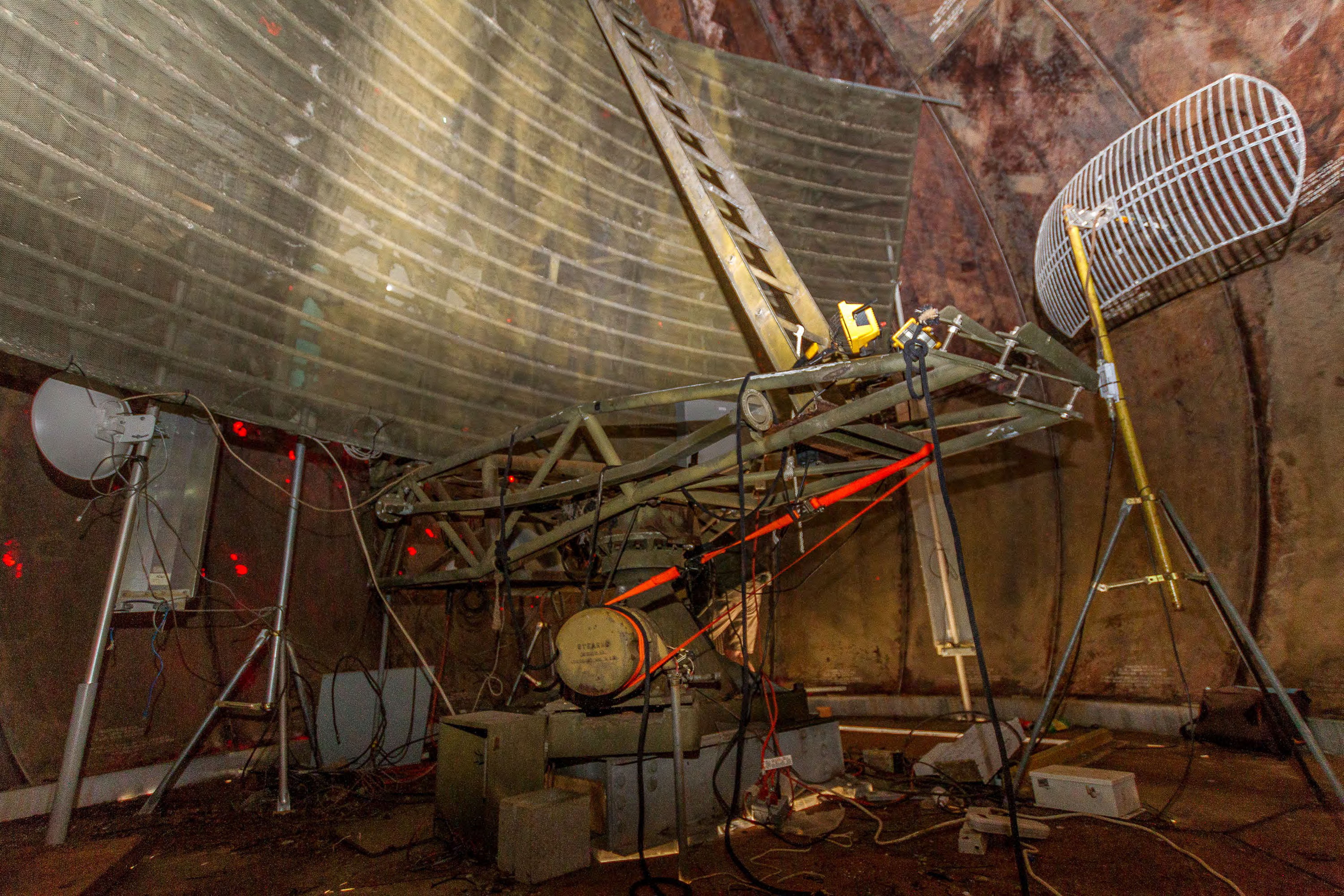 Interior of radome from northwest, relatively modern communications equipment strewn and mounted here and there, sliding door - nearly closed - barely visible as horizontal white line on floor in background